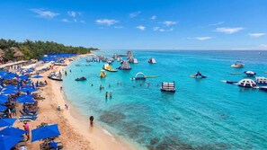 A beach with clear turquoise water, numerous umbrellas, and people enjoying the water.