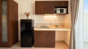 A compact kitchen with a black refrigerator, wooden cabinets, a microwave, and a sink.
