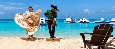 A beach with clear turquoise water, a wooden chair, and a person in traditional attire.
