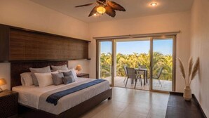 A modern bedroom with a large bed, a ceiling fan, and a view of palm trees through a sliding glass door. - Penthouse by the Sea at The Beach Club Condos (Quintana Roo)
