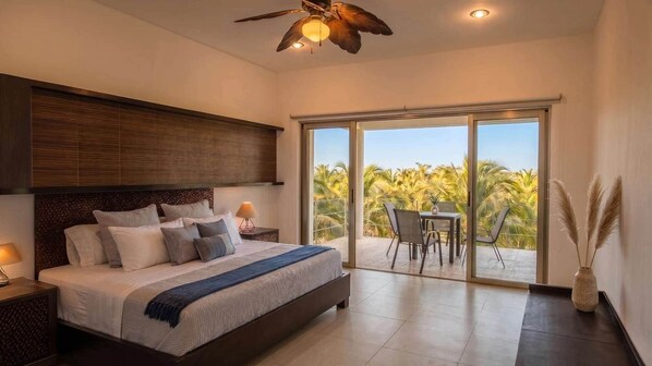A modern bedroom with a large bed, a ceiling fan, and a view of palm trees through the sliding glass door.