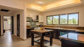 A modern kitchen with a central island, a microwave, and a large window with a view of palm trees.