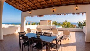 An outdoor patio with a table and chairs, overlooking a pool and the ocean. - Penthouse by the Sea at The Beach Club Condos (Quintana Roo)
