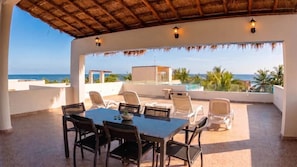 Een terras buiten met een tafel en stoelen, met uitzicht op een zwembad en de oceaan.