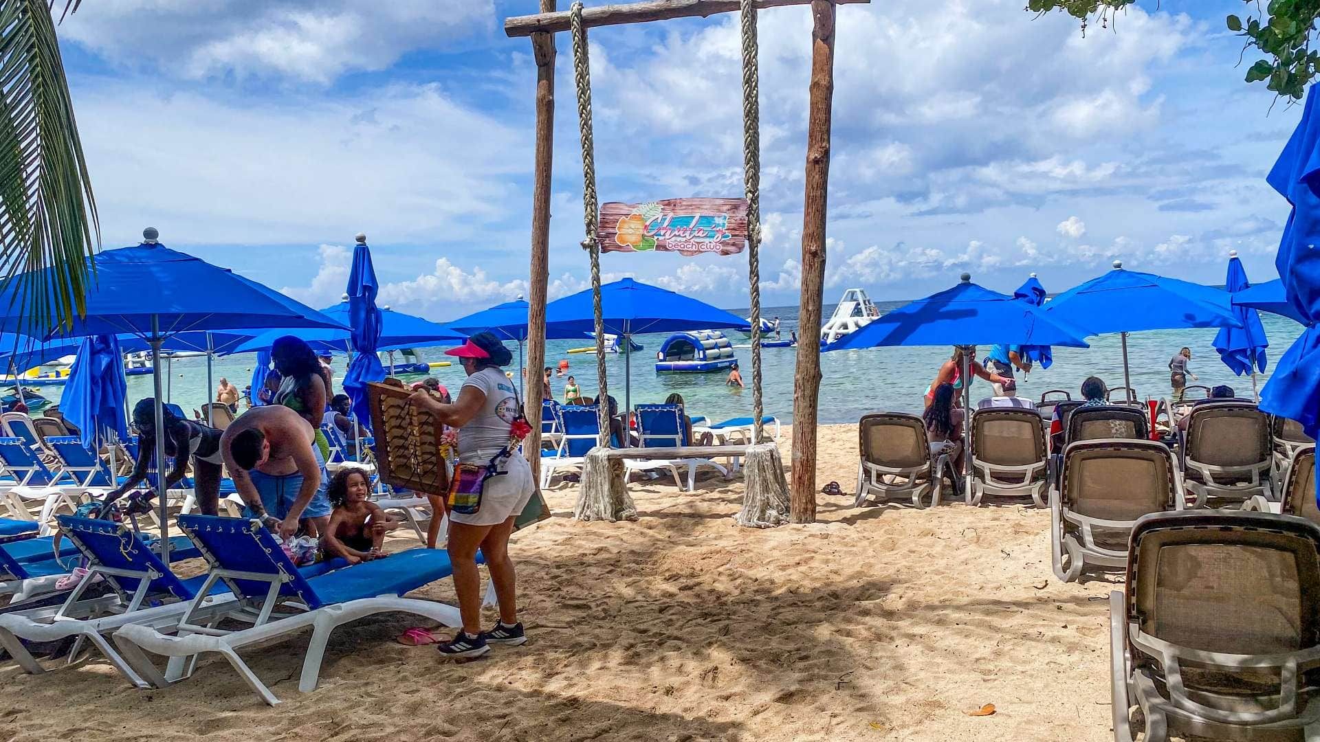 A beach with rows of sun loungers and umbrellas, a wooden swing set, and a sign for 'Chula's Beach Club.'