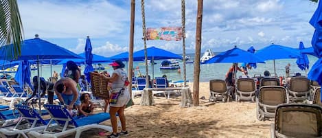 A beach with rows of sun loungers and umbrellas, a wooden swing set, and a sign for 'Chula's Beach Club.'