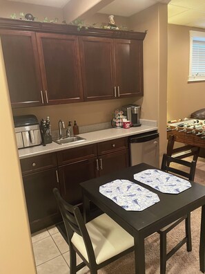 A kitchen with dark wooden cabinets, a coffee maker, and a table with two placemats. - Private Code-Access Suite with Foosball Table (Fort McMurray)