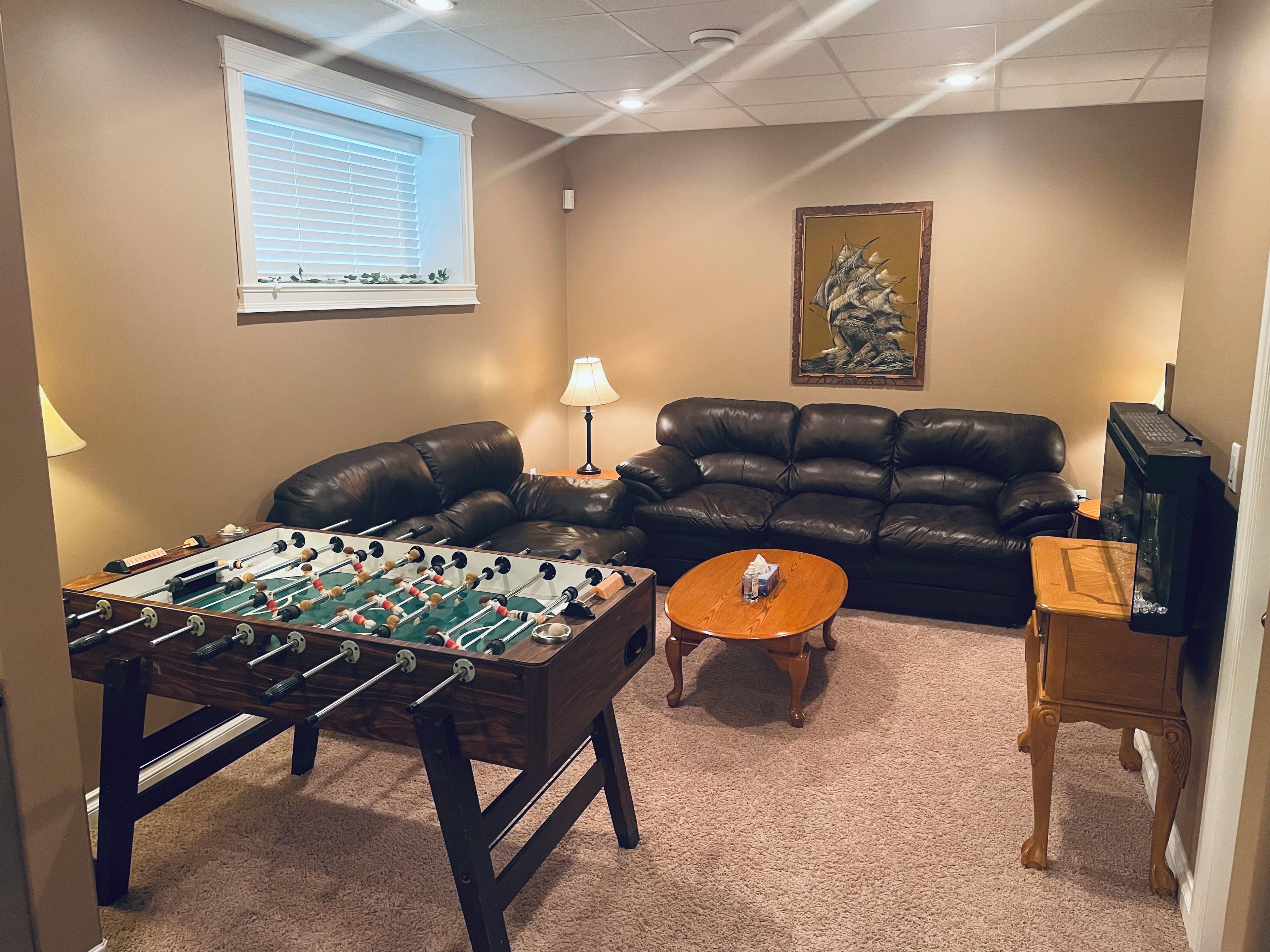 A living room with a foosball table, a leather sofa, a coffee table, and a television.