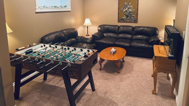 Una sala de estar con mesa de futbolín, sofá de cuero, mesa de centro y televisor.