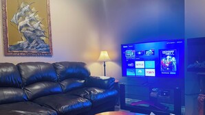 Una sala de estar con un sofá de cuero, una mesa de centro de madera, un televisor que muestra servicios de streaming y una obra de arte enmarcada en la pared.