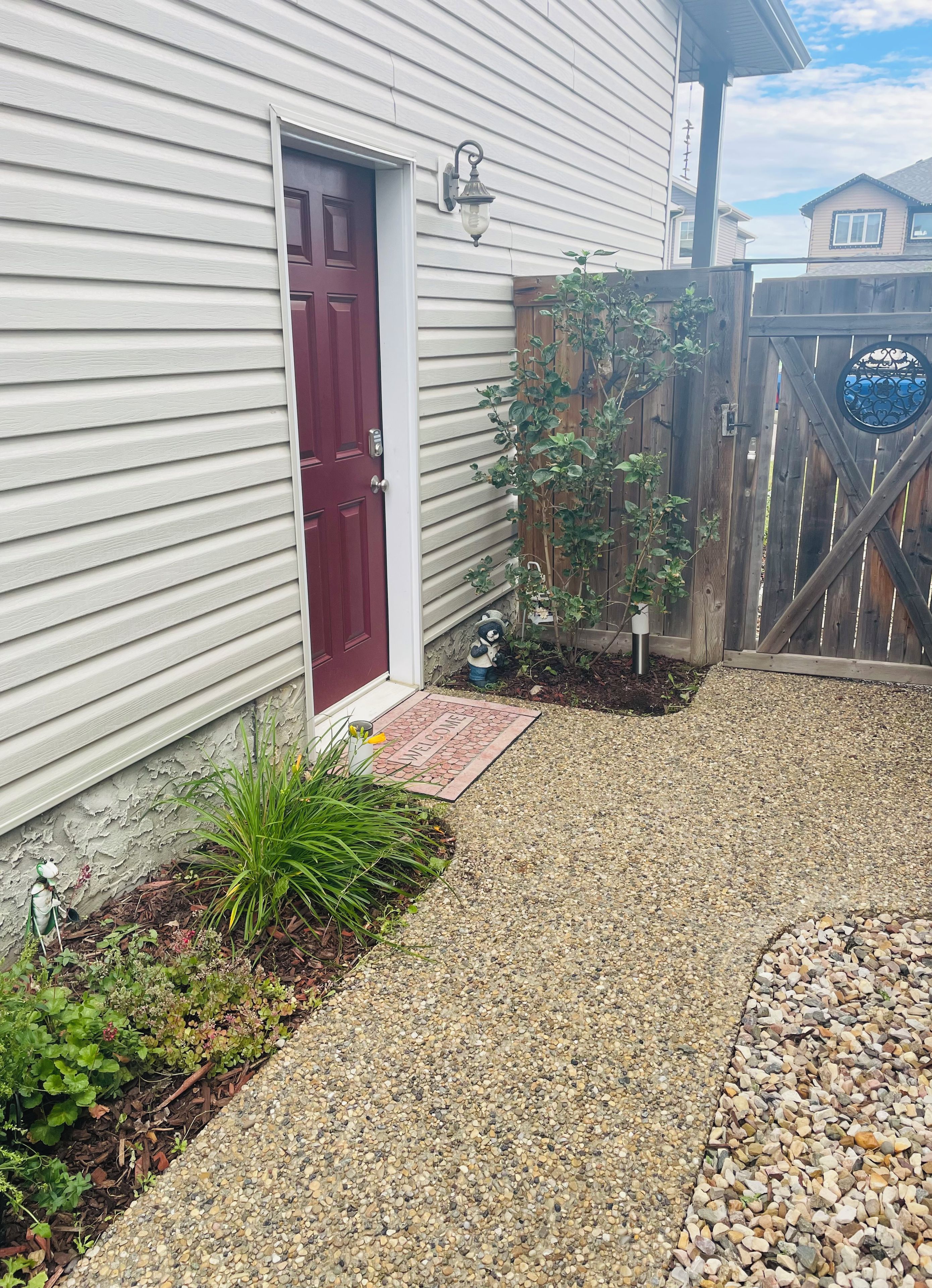 A house with a red door, a welcome mat, a gravel driveway, and a wooden fence.