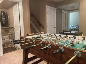 A foosball table in a room with a staircase, a door, and a mirror reflecting a bed. - Private Luxury Code-Access Suite with Foosball Table (Fort McMurray)