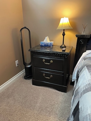 A bedroom with a nightstand, a lamp, a tissue box, and a bed with a striped blanket. - Private Luxury Code-Access Suite with Foosball Table (Fort McMurray)