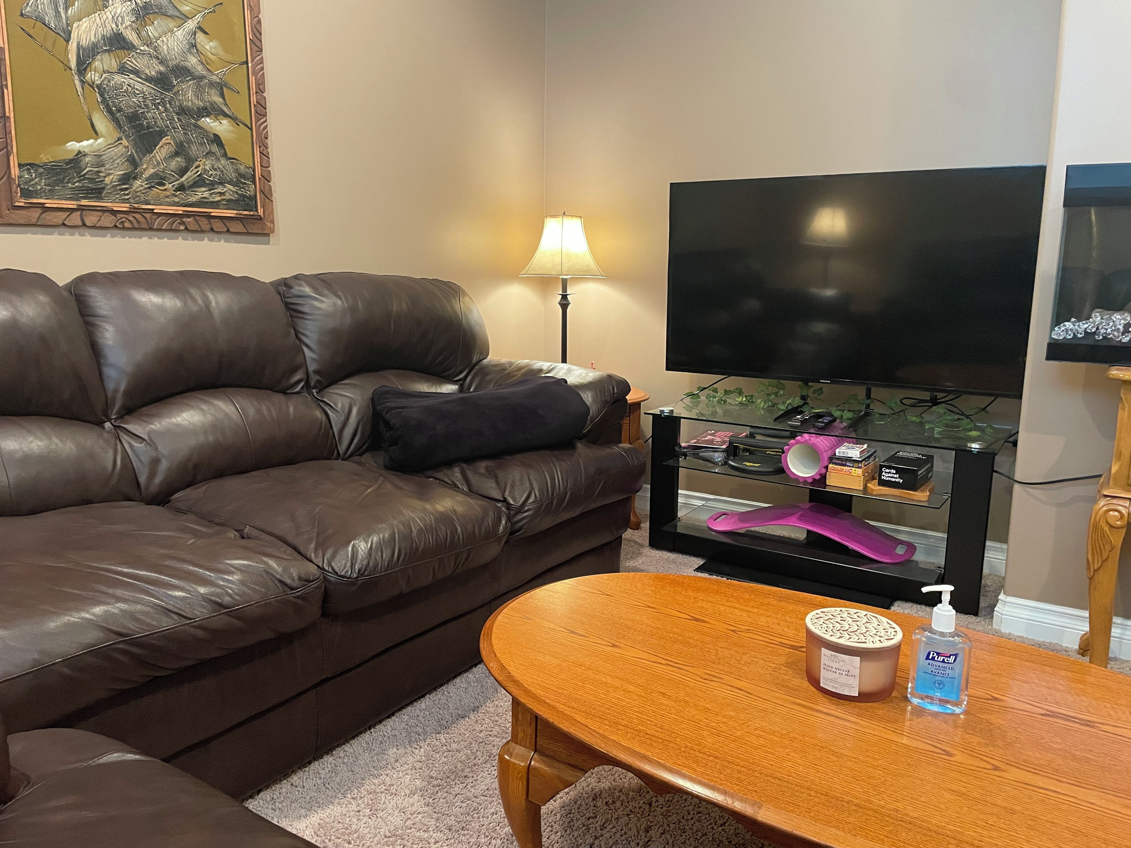A living room with a leather sofa, a flat-screen TV, a glass coffee table, and a lamp.
