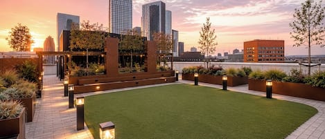 Un jardín en la azotea con un sendero, jardineras y vistas del horizonte de la ciudad.