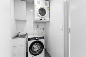 A compact laundry area with a front-loading washing machine and a top-loading dryer. - Beachfront Broadwater & Ocean Views 2BR w/ Parking (Surfers Paradise)
