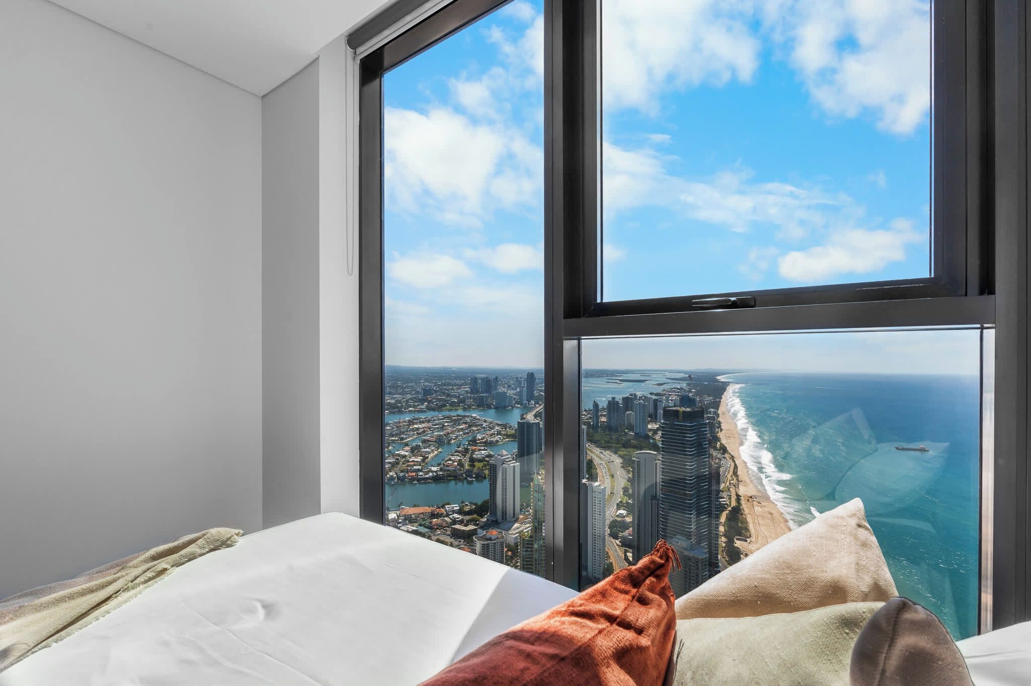 A bedroom with a large window overlooking a coastal cityscape.