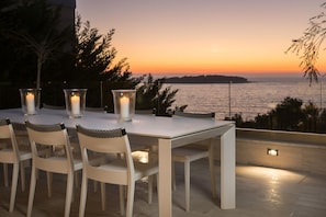 An outdoor dining area with a table and chairs, candles, and a view of the sea at sunset. - Villa Vitomera - Modern villa with pool (Primosten)