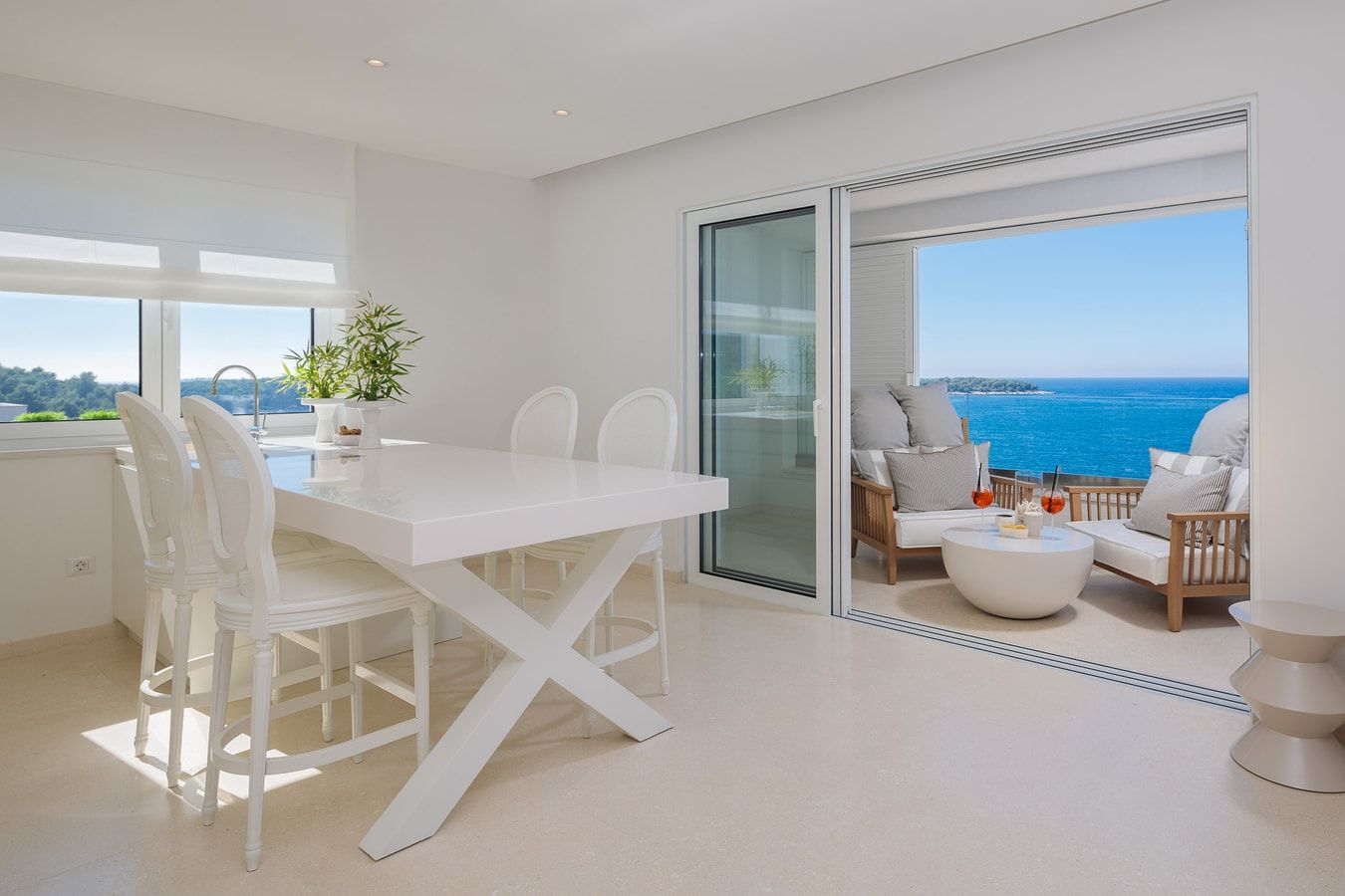 Un interior moderno con una mesa de comedor blanca, sillas y un balcón con vista al mar.