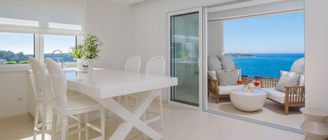 Un interior moderno con una mesa de comedor blanca, sillas y un balcón con vista al mar.