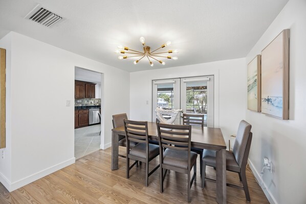 A dining area with a table and chairs, a modern chandelier, and a view through a glass door.
