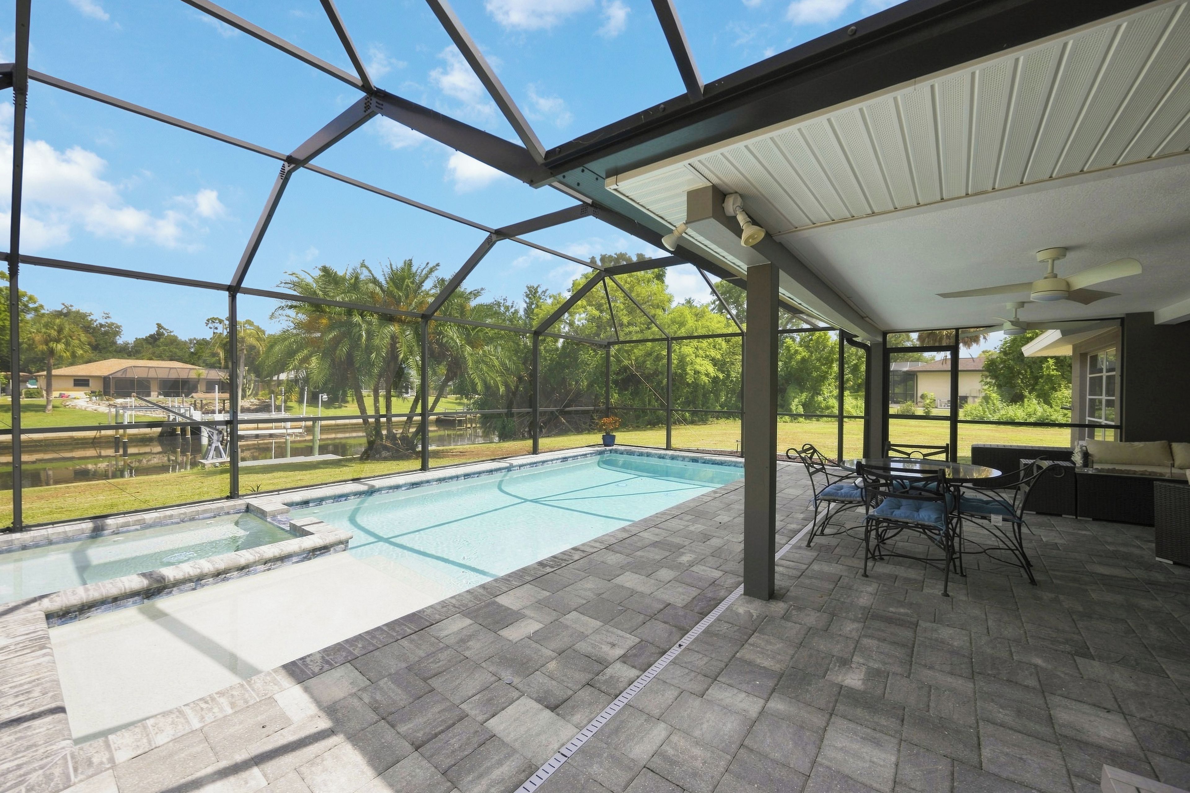 Une piscine intérieure avec vue sur l’extérieur, un patio couvert avec des sièges et un ciel dégagé.