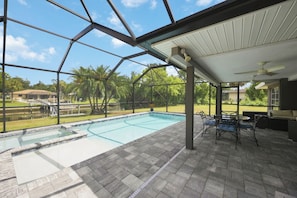 An indoor swimming pool with a view of the outdoors, a covered patio area with seating, and a clear sky.