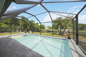 A covered outdoor swimming pool with a view of a residential area and trees. - Waterfront 2BR · Heated Saltwater Pool & Spa · Dock + 10K Boat Lift (Port Charlotte)