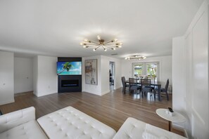 A modern living room with a flat-screen TV, a dining area with a table and chairs, and a unique ceiling light fixture.