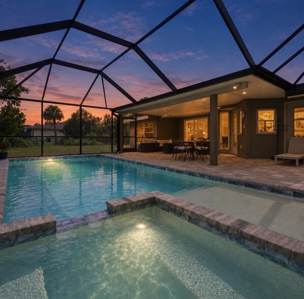 A swimming pool with a covered patio area, clear pool water, and a sunset view.