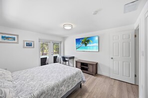 A bedroom with a bed, a desk, a chair, a TV, and a door. - Waterfront 2BR · Heated Saltwater Pool & Spa · Dock + 10K Boat Lift (Port Charlotte)