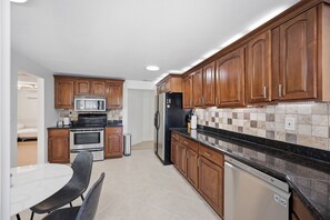 A modern kitchen with wooden cabinets, stainless steel appliances, and a tiled backsplash. - Waterfront 2BR · Heated Saltwater Pool & Spa · Dock + 10K Boat Lift (Port Charlotte)