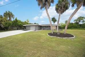 A single-story house with a garage, surrounded by a well-maintained lawn and palm trees.