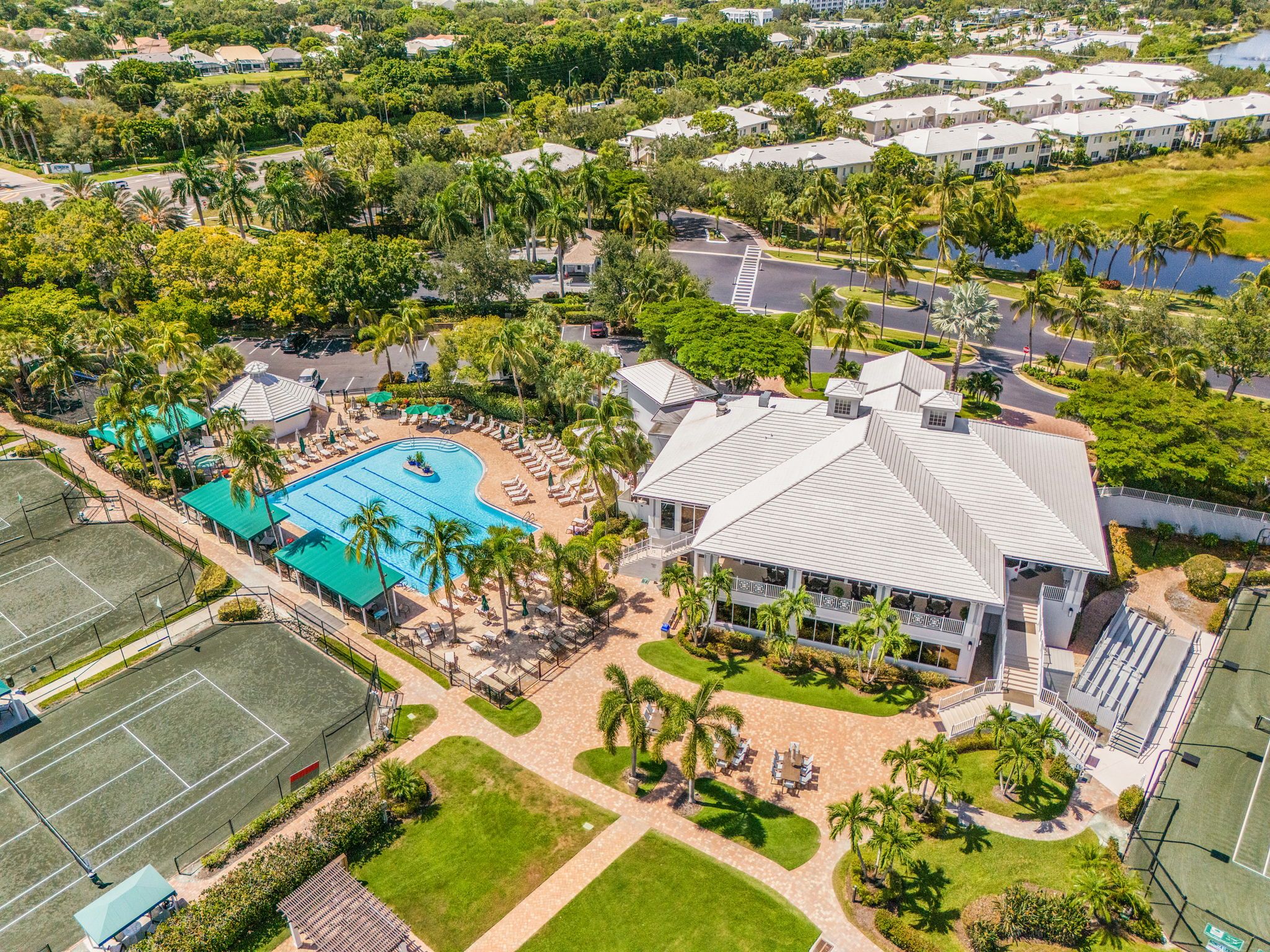 An aerial view of a resort with a swimming pool, tennis courts, and a large building with multiple balconies.