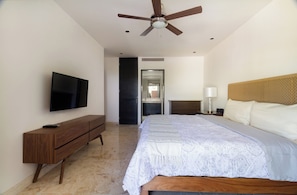 A bedroom with a bed, a TV, a wooden cabinet, a ceiling fan, and a door leading to another room. - Ocean View / Fitness Center / Private Beach / Huge Pool (Playa Del Carmen)