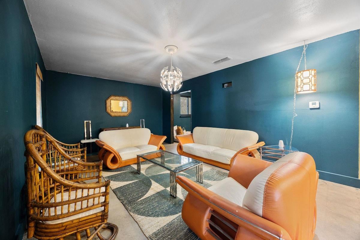 Een woonkamer met een blauwe wand, een houten stoel, twee banken, een glazen salontafel en een hanglamp.