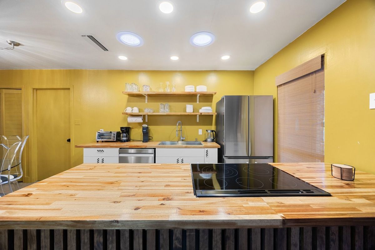 Een moderne keuken met een houten aanrechtblad, roestvrijstalen apparatuur en een gele wand.