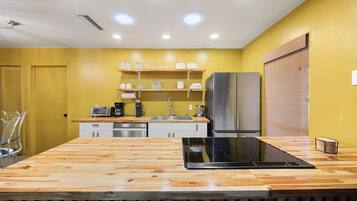 Een moderne keuken met een houten aanrechtblad, roestvrijstalen apparatuur en een gele wand.