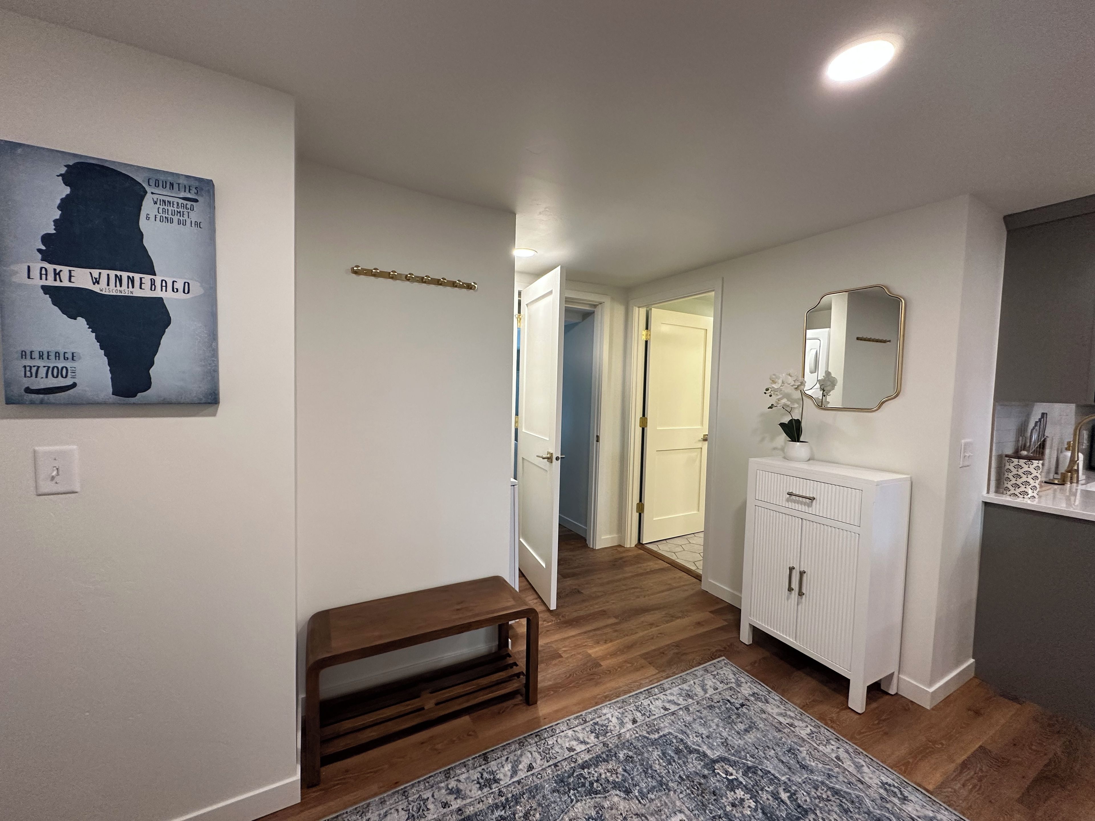 Een gang met een houten bankje, een witte radiator, een spiegel en een vloerkleed.