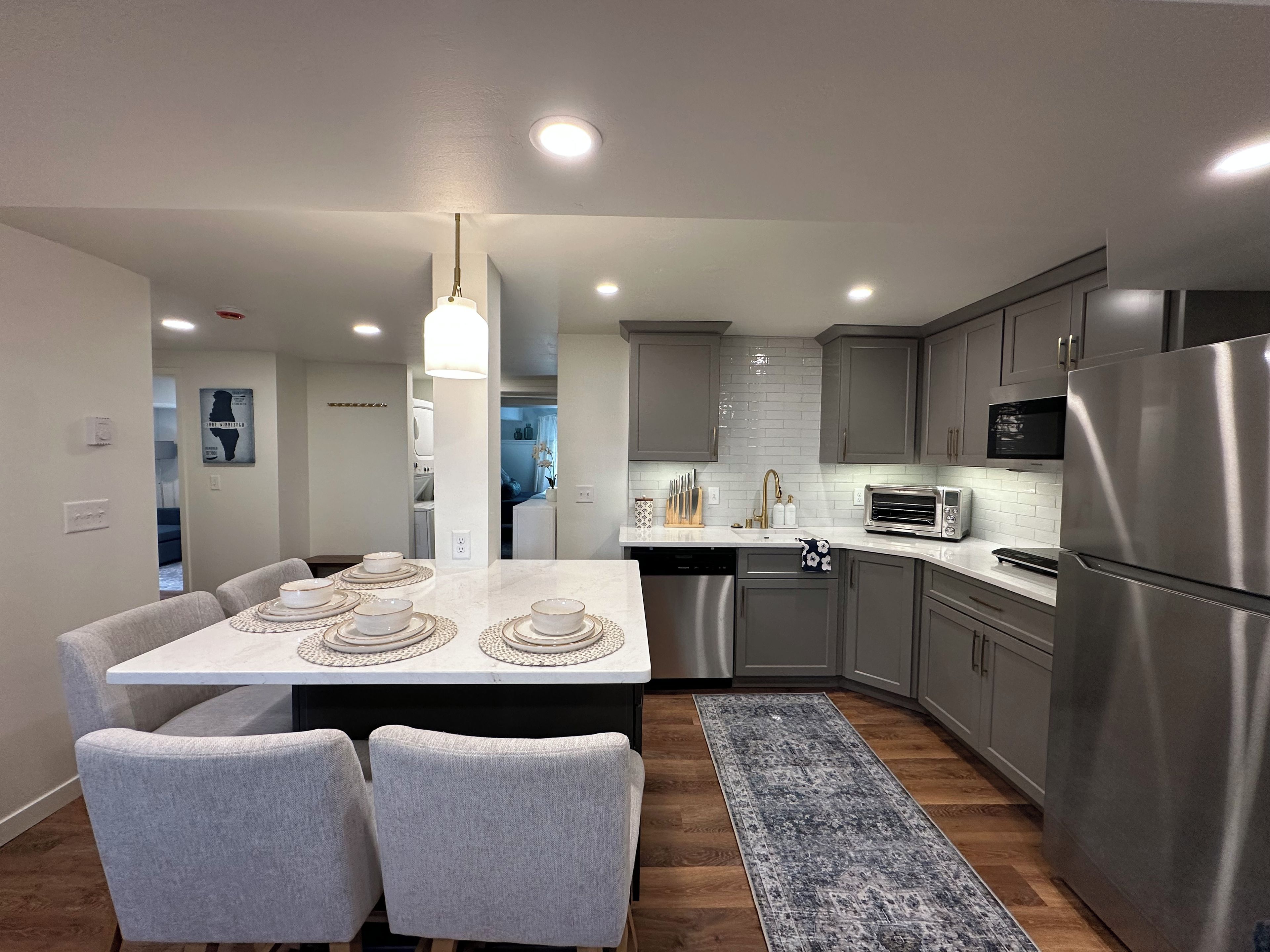 Cocina moderna con armarios grises, electrodomésticos de acero inoxidable y una zona de comedor con mesa blanca y sillas grises.