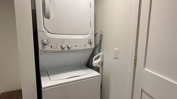 A compact laundry room with a front-loading washer and dryer, a door with a brass handle, and a wooden floor.