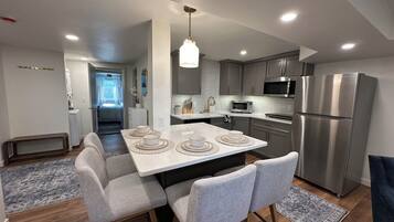 A modern kitchen with a central island, grey cabinets, stainless steel appliances, and a dining area with grey upholstered chairs.
