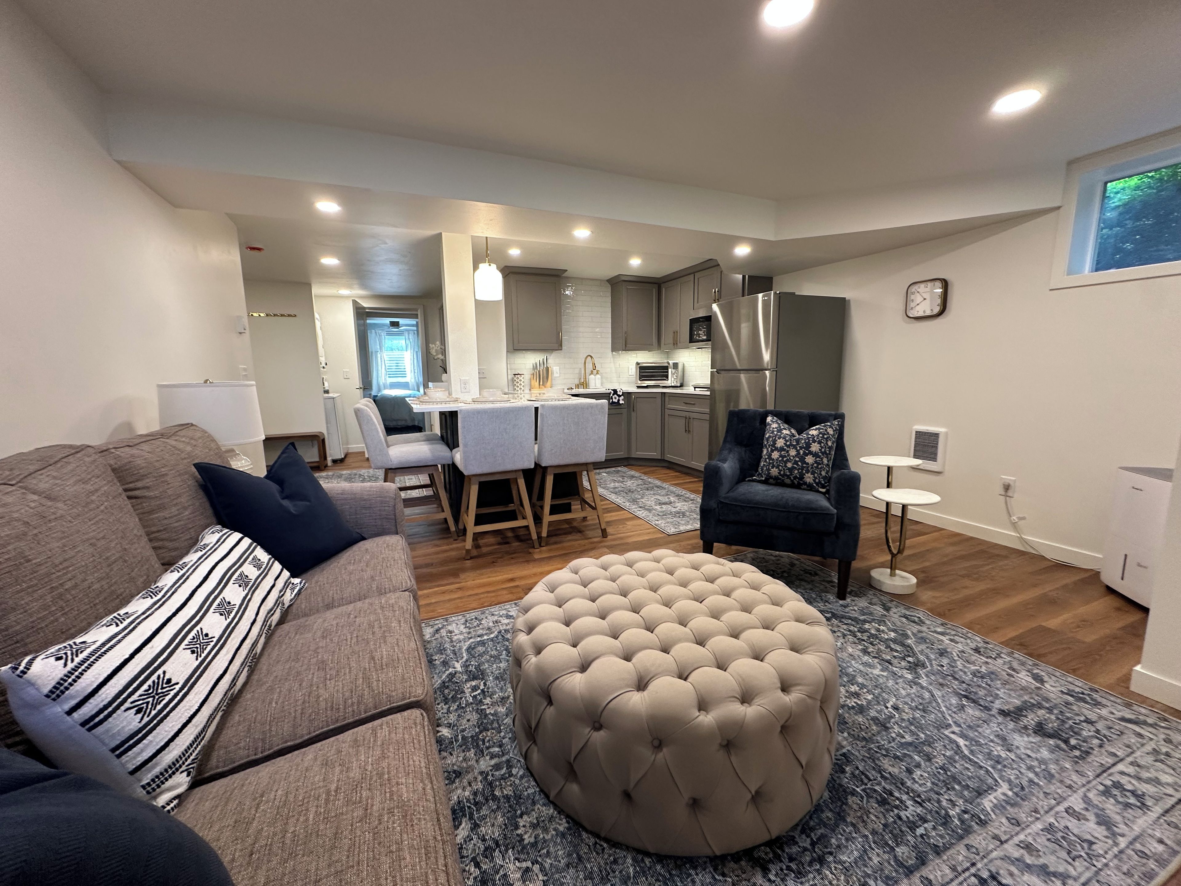 Un salon moderne avec un canapé gris, un pouf rond et un fauteuil foncé.