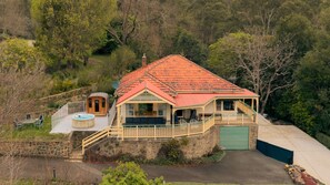 A house with a red roof, a stone foundation, a wooden deck, and a hot tub. - Warburton Stays | Grand View (Warburton)