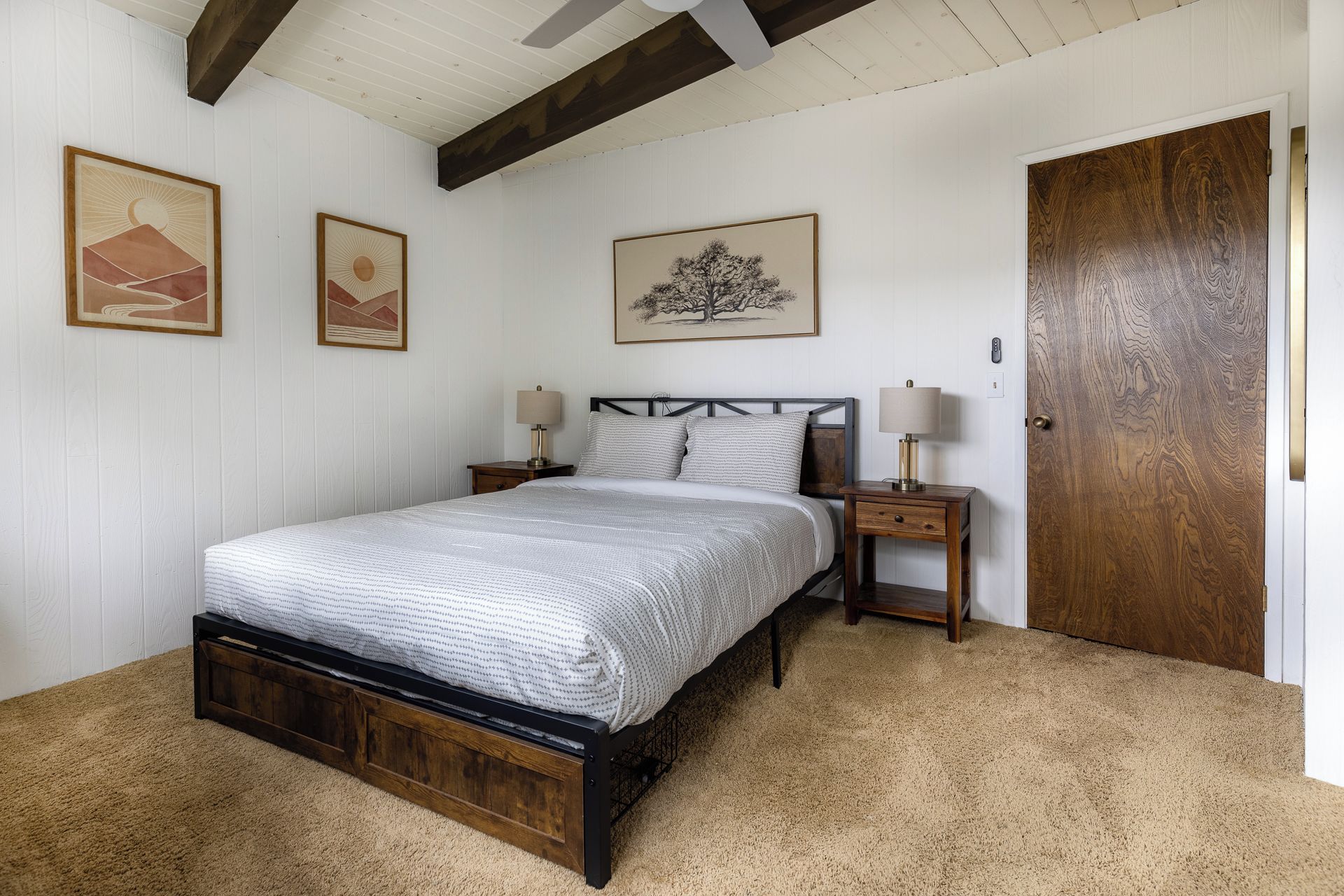 Ein Schlafzimmer mit einem Bett, zwei Nachttischen, einer Holztür und drei gerahmten Kunstwerken an der Wand.