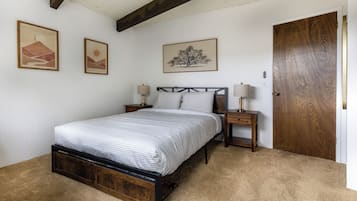 A bedroom with a bed, two bedside tables, a wooden door, and three framed artworks on the wall.
