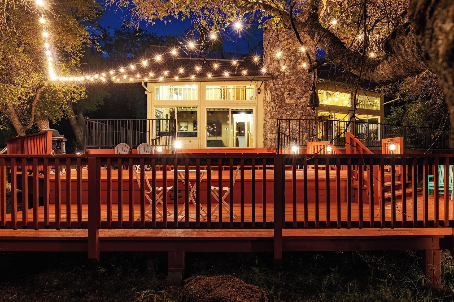 A wooden deck with a railing, a glass door entrance, and string lights.