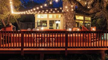 A wooden deck with a railing, a glass door entrance, and string lights.