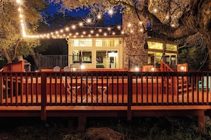Une terrasse en bois avec une rambarde, une porte-fenêtre et des guirlandes lumineuses.