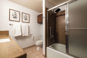 Et badeværelse med badekar, toilet og bruseområde med glasdør. To billeder hænger på væggen og to håndklæder på håndklædestangen.